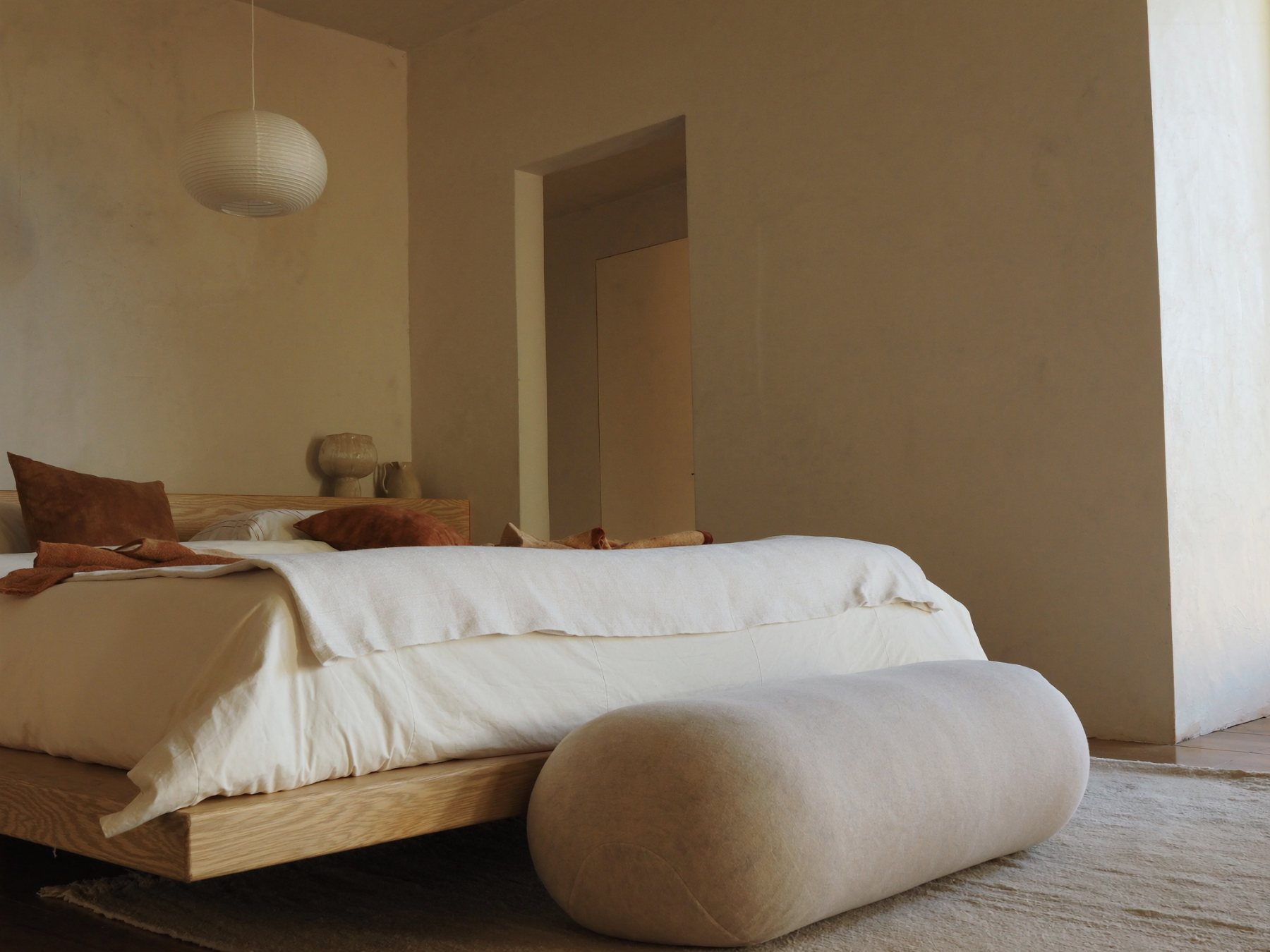 Serene bedroom with low oak bed, ivory linen and lime wash walls
